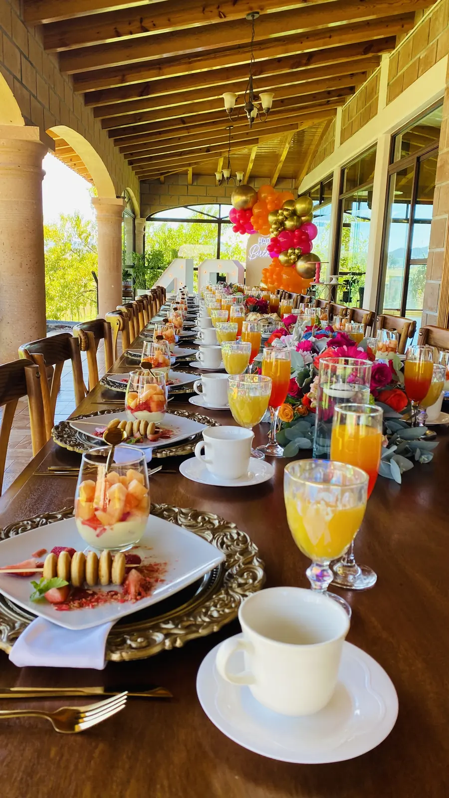Mesa de desayuno con fruta, jugos y café bajo arcos